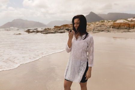 Side view of young woman talking on mobile phone at beach in the sunshine