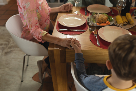 Close up of hands of family praying together before having meal on dining table at homeの写真素材