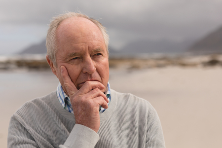 Front view of active senior man standing on the beach with mountains in the background. He seens relaxedの写真素材