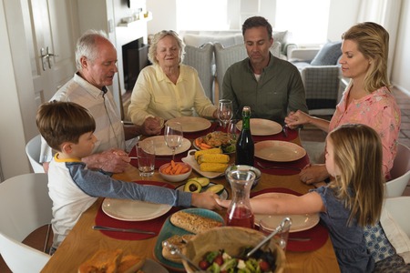 front view of a multi-generation family praying together before having meal on dining table at home