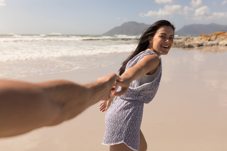 Front view of a happy young couple holding hands on beach in the sunshineの写真素材