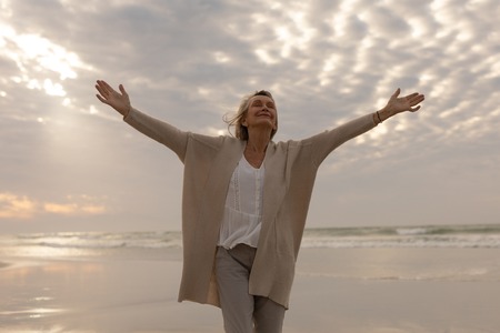 Front view of active senior Caucasian woman standing with arms outstretched on the beachの写真素材