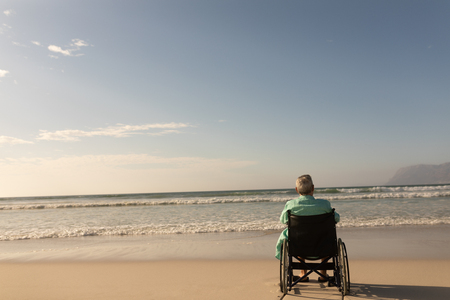 Rear view of disabled senior man looking at ocean on the beachの写真素材