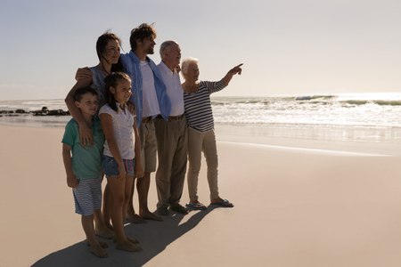 Side view of senior woman with her family pointing at distance on beach in the sunshineの写真素材
