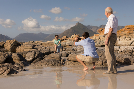 Father clicking photo of his son with mobile phone on beach in the sunshineの写真素材
