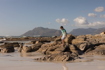 Boy walking on rocks at beach in the sunshine