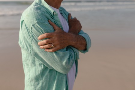 Mid section of senior man standing with arms crossed on the beachの写真素材