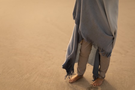 Low section of active senior Caucasian woman wrapped in a shawl standing on the beachの写真素材