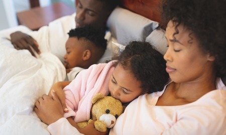 Close-up of African American family sleeping together on bed in bedroom at homeの写真素材