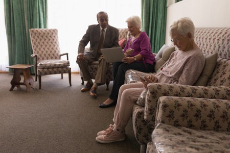 Side view of senior friends using digital tablet and laptop on sofa at homeの写真素材