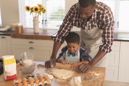 Front view of African American father and son rolling out cookie dough in kitchen at homeの写真素材