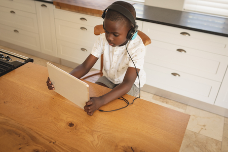 High angle view of African American boy playing game on digital tablet at dining table in kitchen at homeの写真素材