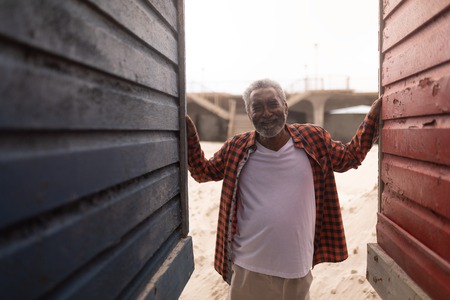 Front view of happy senior man standing between beach huts at beachの写真素材