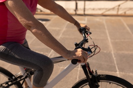Mid section of senior woman riding a bicycle on a promenade at beach