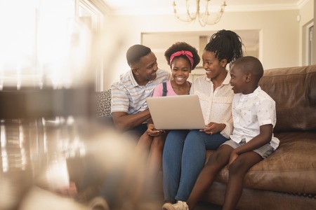 Front view of happy African American family sitting on the sofa and using laptop at homeの写真素材