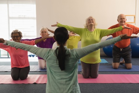 Young female trainer assisting senior people with tensioned arms in fitness studio