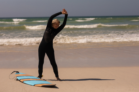 Front view of active senior female surfer with surfboard exercising on the beachの写真素材