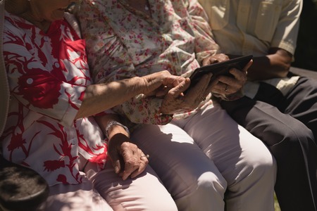 Mid section of senior friends using digital tablet in garden on a sunny dayの写真素材