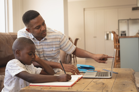 Side view of African American father helping his son with homework on laptop at table in a comfortable homeの写真素材