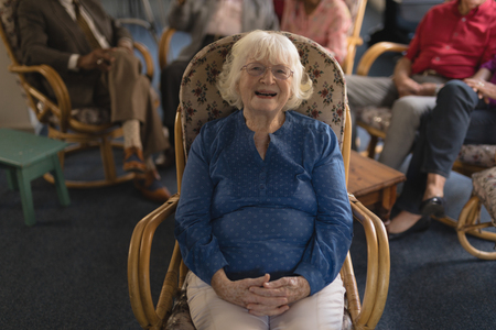 Front view of happy senior woman with hand clasped, sitting and looking at camera in nursing homeの写真素材