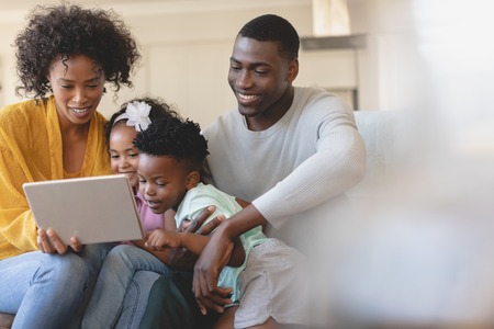 Front view of happy African American parents with their cute children using digital tablet on sofa in a comfortable homeの写真素材