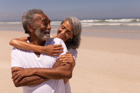 Front view of happy senior woman embracing senior man on beach in the sunshineの写真素材