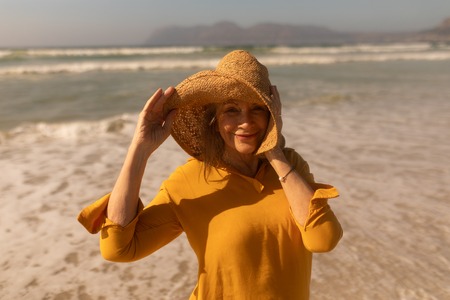 Portrait of active senior woman in hat standing on the beachの写真素材
