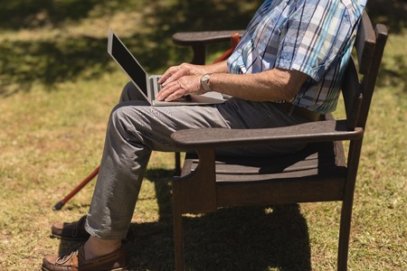 Low section of senior man using laptop while sitting on a bench in the park