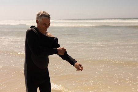 Side view of active senior male surfer wearing wet suit on the beach