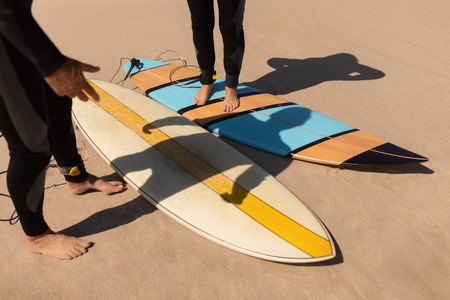 Low section of senior surfer couple standing with surfboard on the beachの写真素材