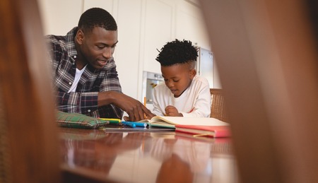 Front view of African American father helping his son with homework at table in a comfortable home