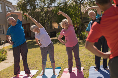 Front view of trainer training senior motivated people in performing yoga in the parkの写真素材