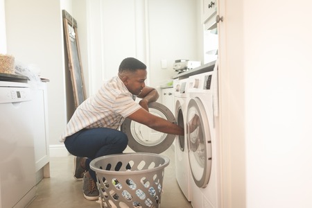 Side view of African American man washing clothes in washing machine at home