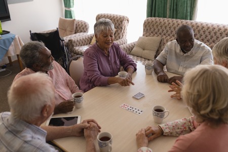 High angle view of group of senior people playing cardsand taking coffee around a table in living...