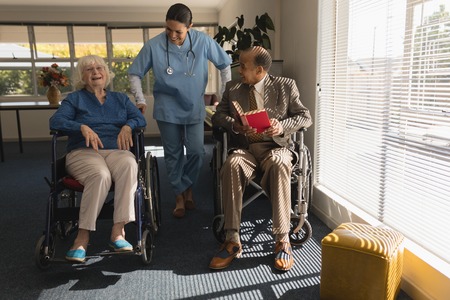 Front view of happy female doctor talking with disable senior couple at homeの写真素材