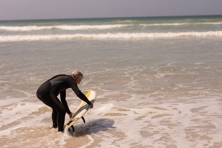 Side view of senior male surfer with surfboard surfing in sea on a sunny dayの写真素材
