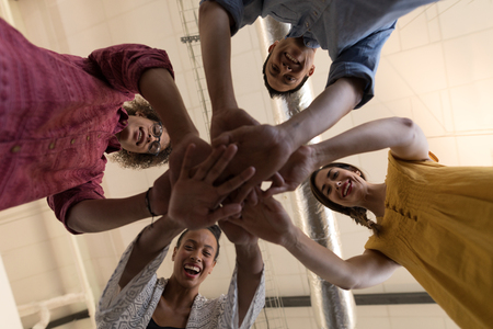 Low angle view of diverse casually dressed business colleagues forming hand stack and smiling in...