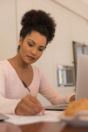 Front view of African American beautiful woman filling a form while using laptop at homeの写真素材