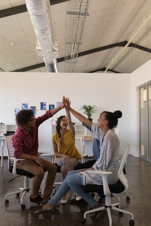 Front view of happy multi-ethnic business colleagues giving high five to each other in modern office