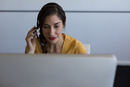 Front view of pretty mixed-race female executive looking focused while talking on headset in modern officeの写真素材
