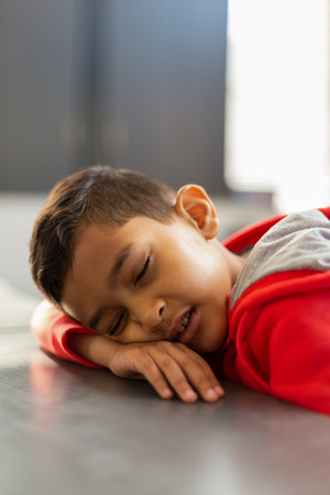 Close-up of cute mixed-race schoolboy sleeping with mouth open at desk in a classroom at elementary schoolの写真素材