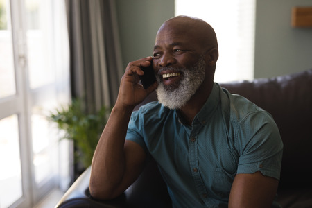 Front view of senior man talking on mobile phone in living room at home