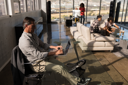 Side view of male executive working on laptop in modern office with business team working in the backgroundの写真素材