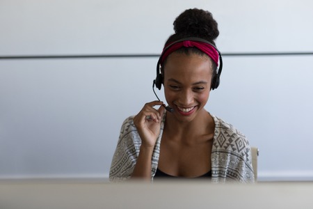 Front view of pretty mixed-race female executive talking on headset in modern office
