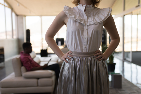 Mid section of well dressed Caucasian female executive standing with hands on hip in officeの写真素材