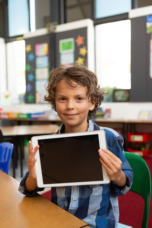 Front view of a Caucasian schoolboy holding digital tablet and looking at the camera in the library at schoolの写真素材