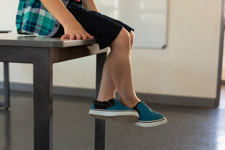 Low section of Caucasian boy sitting over desk in a classroom at elementary school