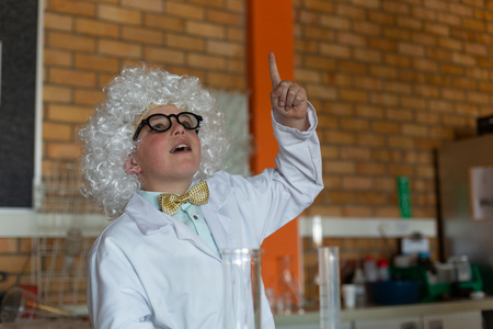Front view of a Caucasian schoolboy in white wig raising hand in laboratory at schoolの写真素材