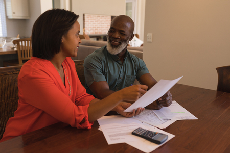 Side view of an active senior couple discussing over invoices in the living room at homeの写真素材