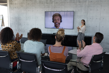 Rear view of young multi-ethnic business colleagues applauding while attending a video call in a...